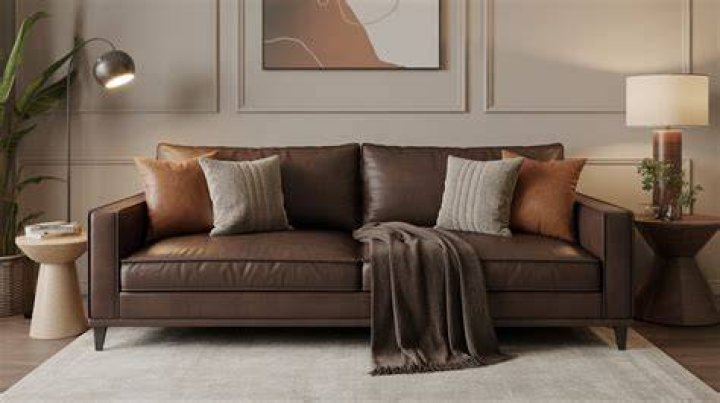 room with a brown sofa and chairs sitting in front of a large window in a wooded area